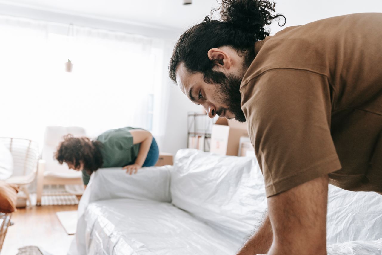 A couple is wrapping furniture in a bright apartment as they get ready to move.