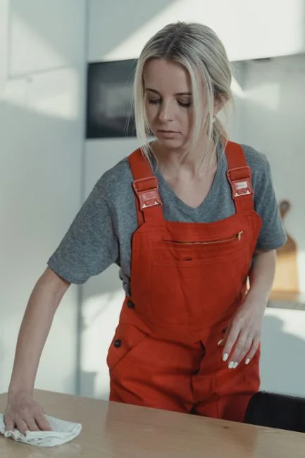 A woman is carefully covering a sofa with protective wrapping while packing boxes in a bright room.